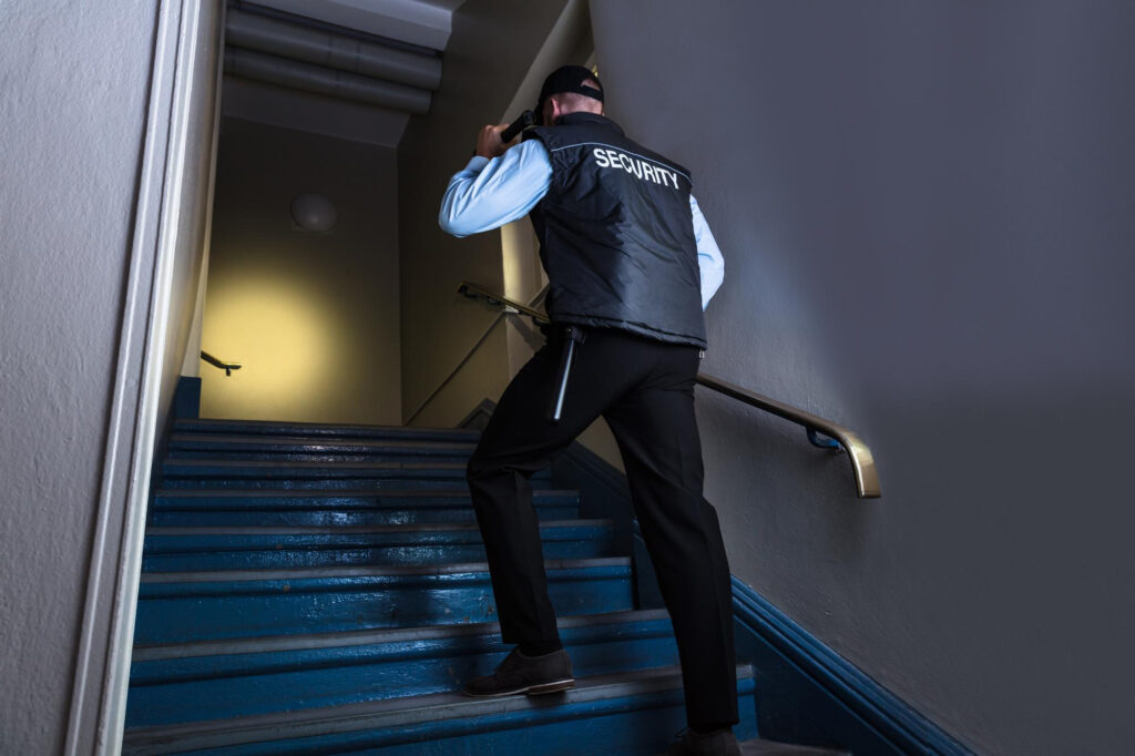 Sicherheitsmitarbeiter kontrolliert mit Taschenlampe ein Treppenhaus – Streifendienst von Secure Time